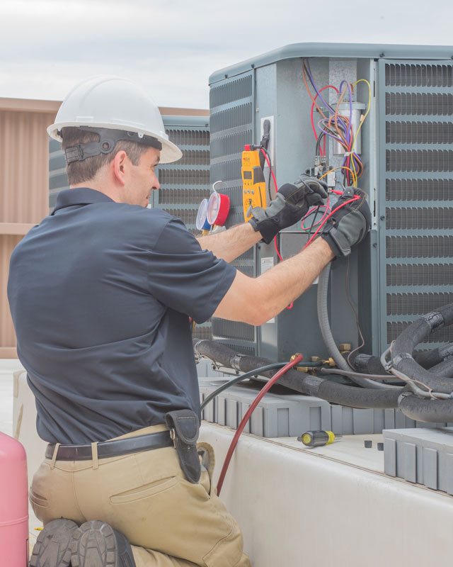 A Triangle Contractor employee performing commercial HVAC maintenance on an outdoor central air conditioner.